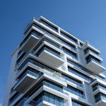 Striking low-angle shot of a modern condominium with unique balcony design and clear blue sky.